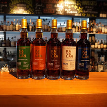 Lade das Bild in den Galerie-Viewer, Fünf Kavalan Solist Whiskyflaschen in verschiedenen Sorten stehen nebeneinander auf einer Holztheke vor einer Bar mit vielen Flaschen im Hintergrund